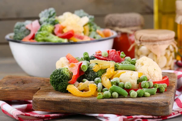 Verdure congelate sul tagliere, sul tovagliolo, sullo sfondo del tavolo di legno — Foto Stock