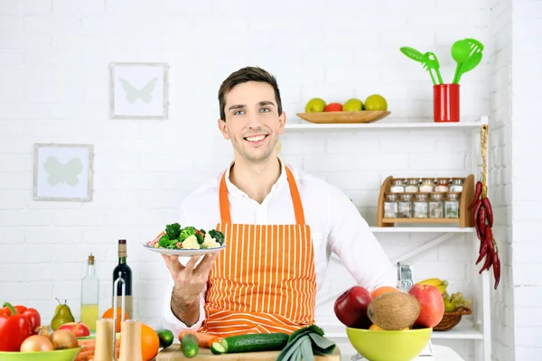 Hombre en la mesa con diferentes productos y utensilios en la cocina sobre fondo de pared blanco —  Fotos de Stock