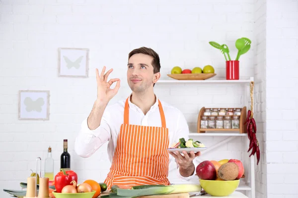 Чоловік за столом з різними продуктами та посудом на кухні на фоні білої стіни — стокове фото