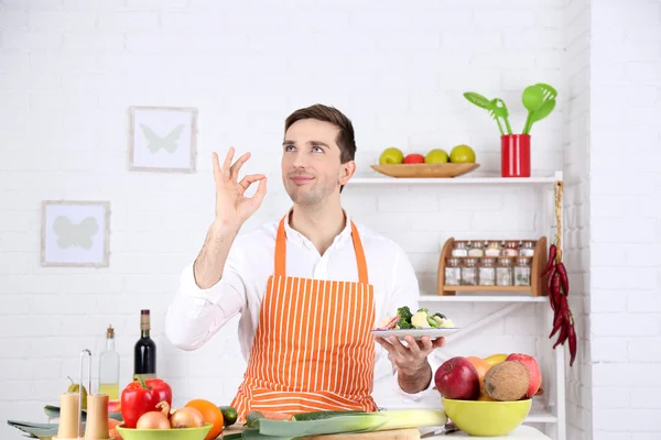 Homem à mesa com diferentes produtos e utensílio na cozinha no fundo da parede branca — Fotografia de Stock