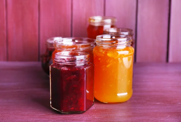 Homemade jars of fruits jam on color wooden background — Stock Photo, Image