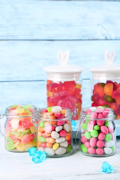 Многоцветные конфеты в стеклянных банках на фоне цвета дерева — стоковое фото