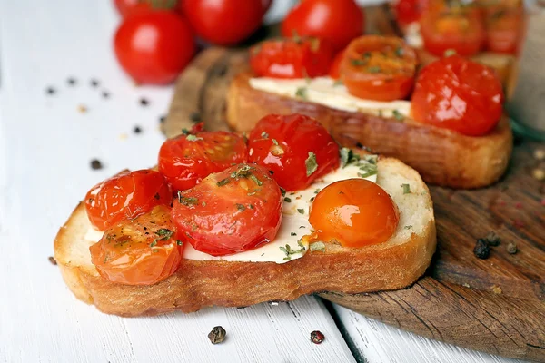 Fette di pane bianco tostato con burro e pomodori in scatola su sfondo tavole di legno di colore — Foto Stock