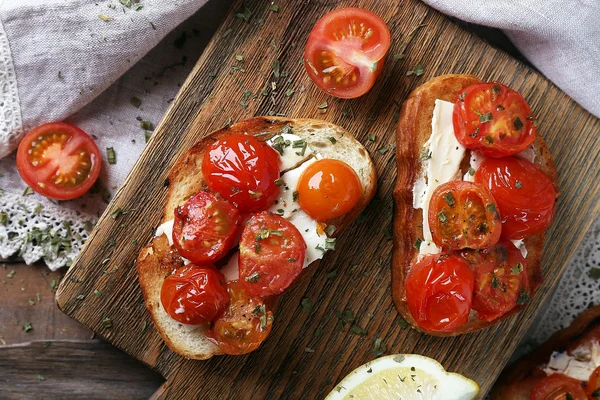 Fette di pane bianco tostato con pomodori in scatola e lime sul tagliere su sfondo tavolo di legno — Foto Stock