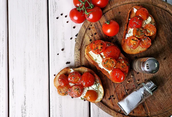 Fette di pane bianco tostato con burro e pomodori in scatola su sfondo tavole di legno di colore — Foto Stock