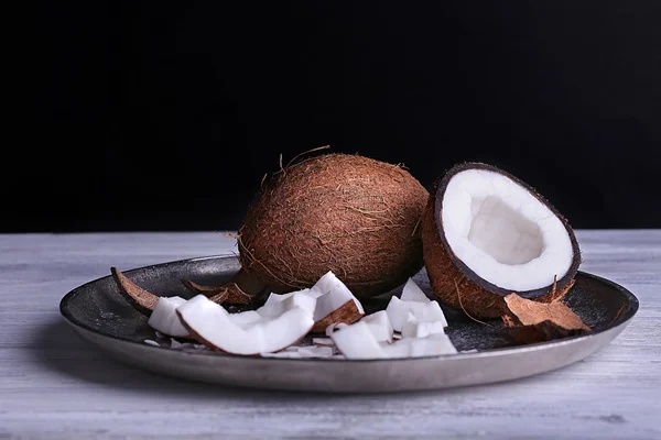 Трещины кокосового ореха на металлической пластине на цветном деревянном столе и темном фоне — стоковое фото