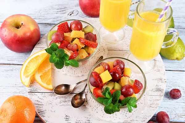 Insalata di frutta con menta e succo d'arancia in bicchieri su sfondo di legno a colori — Foto Stock