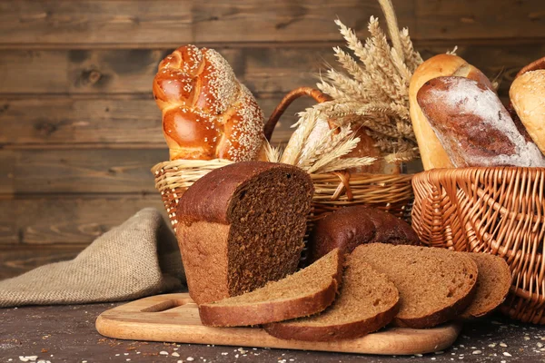 Different bread with ears in basket on wooden background — Stock Photo, Image