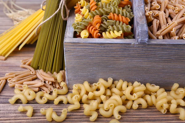 Verschillende soorten pasta in vak op houten achtergrond — Stockfoto