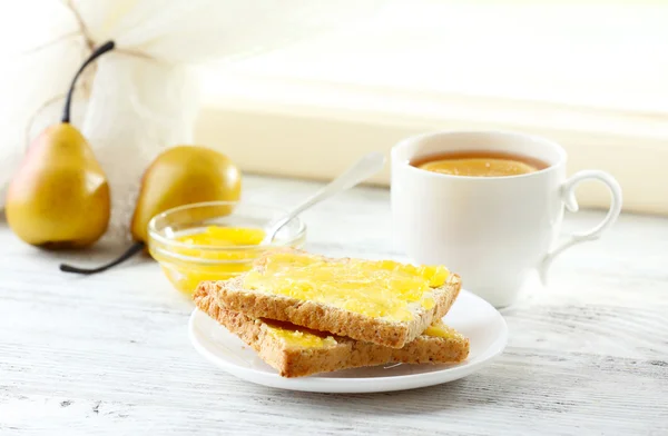 Pane tostato con miele sul piatto e tazza di tè su sfondo chiaro — Foto Stock
