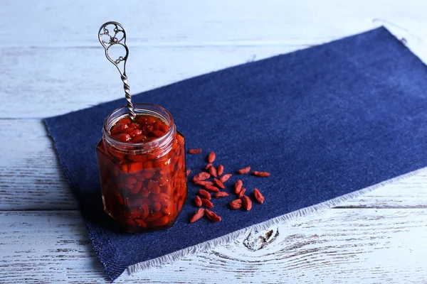 Jar of goji berry jam on napkin on wooden background — Stock Photo, Image