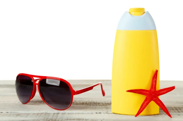 Flasche Sonnencreme mit Sonnenbrille und Seestern auf Tisch isoliert auf weiß — Stockfoto