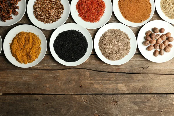 Different spices on plates, on old wooden table — Stock Photo, Image