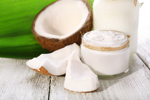 Fresh coconut oil in glass bottle and green leaf on color wooden table background