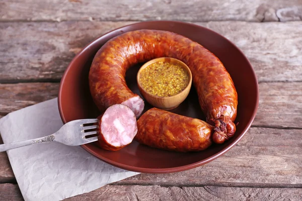 Smoked sausage with mustard on plate on wooden table background — Stock Photo, Image