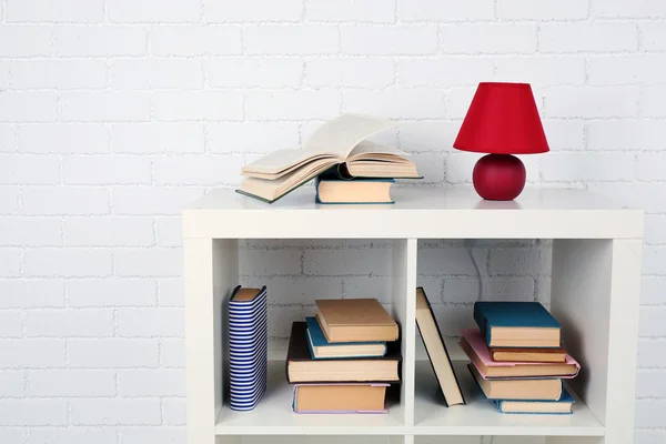 Houten plank met boeken en lamp op bakstenen muur achtergrond — Stockfoto