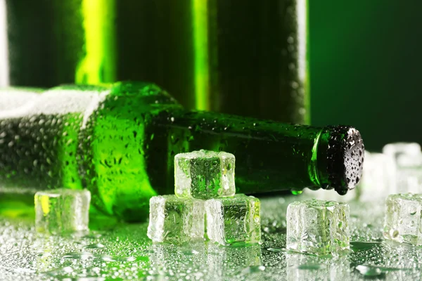 Glasflaskor av öl med isbitar på våta bordet på mörk bakgrund — Stockfoto