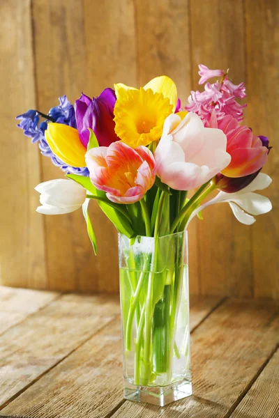 Schöne Frühlingsblumen in Glasvase auf Holzgrund — Stockfoto