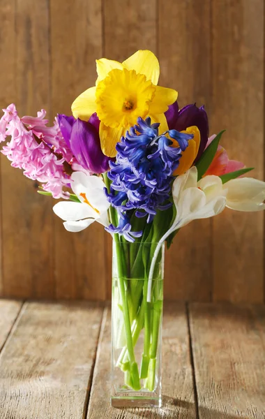 Schöne Frühlingsblumen in Glasvase auf Holzgrund — Stockfoto