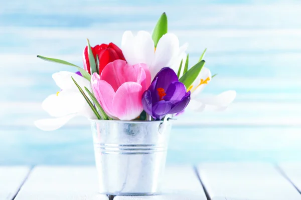 Beautiful spring flowers in metal bucket on color background — Stock Photo, Image