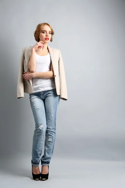 Hermosa joven con chaqueta y jeans posando sobre fondo claro — Foto de Stock