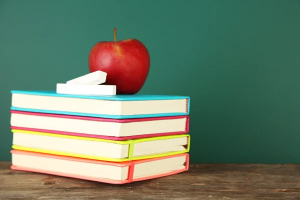 Books, apple and chalk on blackboard background