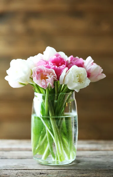 Schöne Tulpen in Glasvase auf Holzgrund — Stockfoto