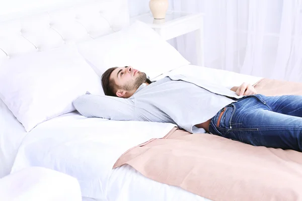 Tired man resting on bed in room — Stock Photo, Image