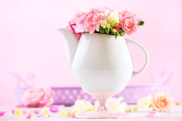 Composición con hermosas flores de primavera en tetera sobre fondo rosa claro — Foto de Stock