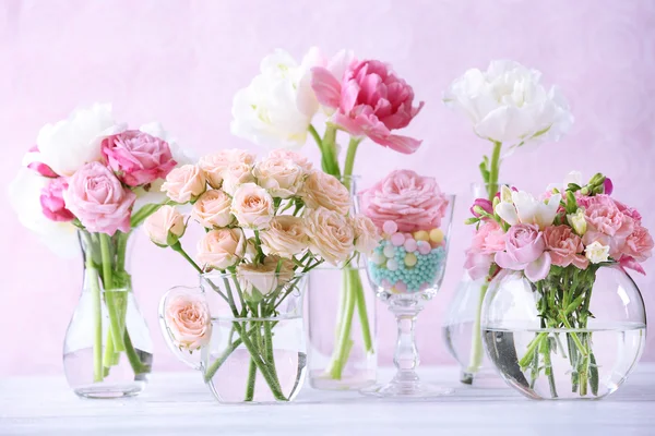 Beautiful spring flowers in glass vases on light pink background