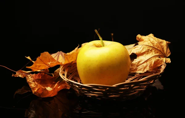 Pomme dans un panier en osier avec feuilles séchées sur fond noir — Photo