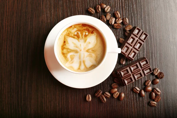 Taza de café latte art con granos y barra de chocolate sobre fondo de madera — Foto de Stock