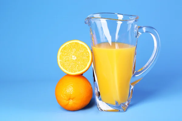 Jarra de cristal de jugo de naranja sobre fondo azul — Foto de Stock