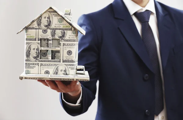 Model of house made of money in male hands on gray background — Stock Photo, Image