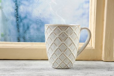 Cup of hot drink on windowsill on rain background clipart