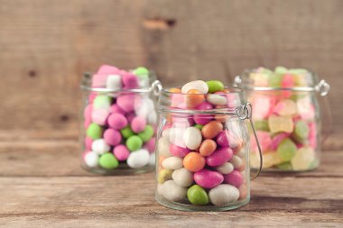 Ahşap arka plan üzerinde cam kavanozlara çok renkli şekerler