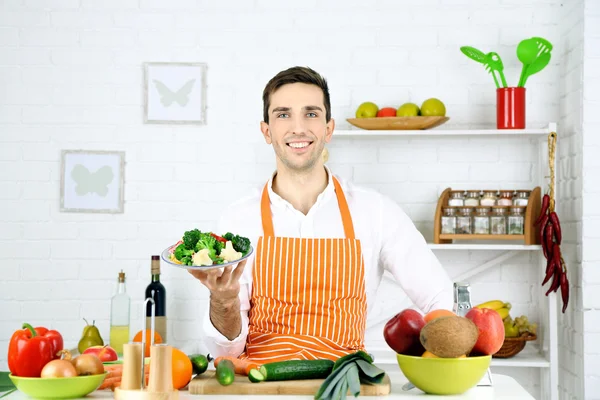 Uomo a tavola con diversi prodotti e utensili in cucina su sfondo bianco a parete — Foto Stock