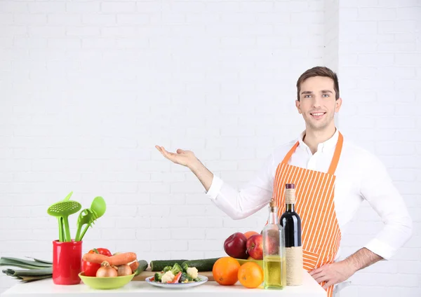 Mann am Tisch mit verschiedenen Produkten und Utensilien in der Küche auf weißem Wandhintergrund — Stockfoto