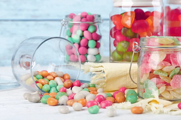 Multicolor snoepjes in glazen potten op een houten achtergrond kleur — Stockfoto