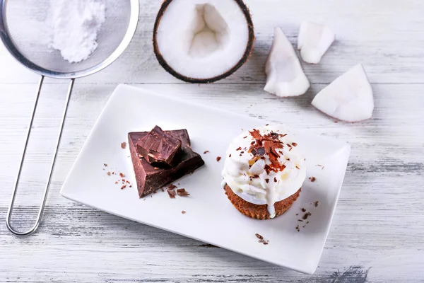 Delicious coconut cupcake with cream and chocolate chips on color wooden table background — Stock Photo, Image