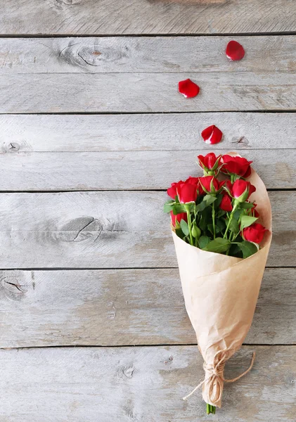 Rote Rosen in Papier gewickelt auf hölzernem Tischhintergrund — Stockfoto