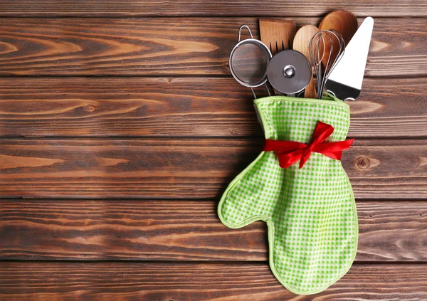 Set of kitchen utensils in mitten on wooden planks background — Stock Photo, Image