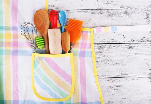 Set of kitchen utensils in pocket of apron on wooden background — Stock Photo, Image