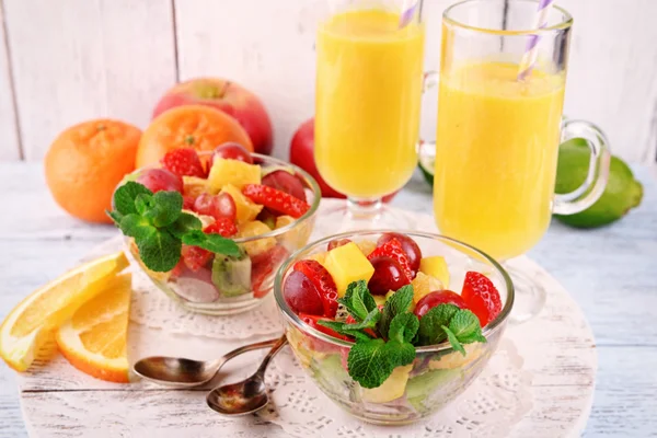 Insalata di frutta con menta e succo d'arancia in bicchieri su sfondo di legno a colori — Foto Stock