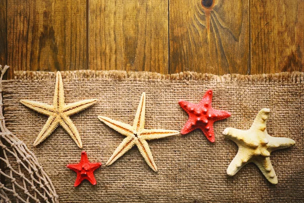 Estrelas do mar em pano de saco em fundo de madeira — Fotografia de Stock