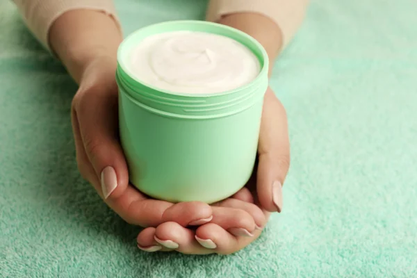 Manos femeninas con tarro de crema sobre fondo de tela — Foto de Stock