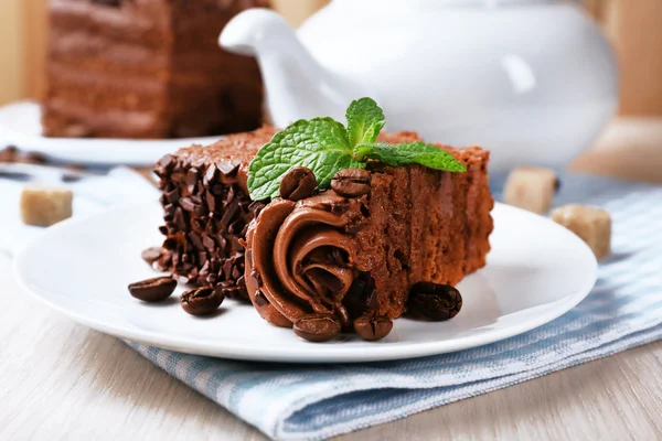 Tasty piece of chocolate cake with mint and cinnamon on wooden table and blurred planks background, closeup view — Stock Photo, Image