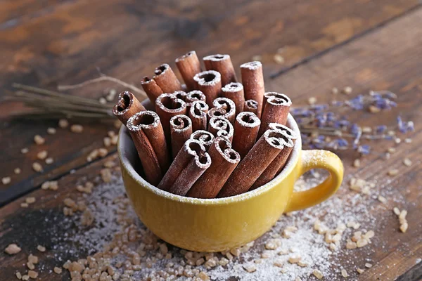 Cinnamon sticks in cup with sugar and lavender on wooden table background — Stock Photo, Image