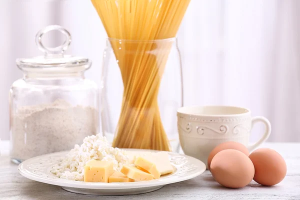 Pasta con productos de diario, harina y huevos sobre mesa de madera sobre fondo cortina — Foto de Stock