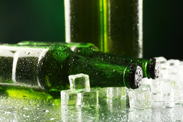 Glasflaschen Bier mit Eiswürfeln auf nassem Tisch auf dunklem Hintergrund — Stockfoto